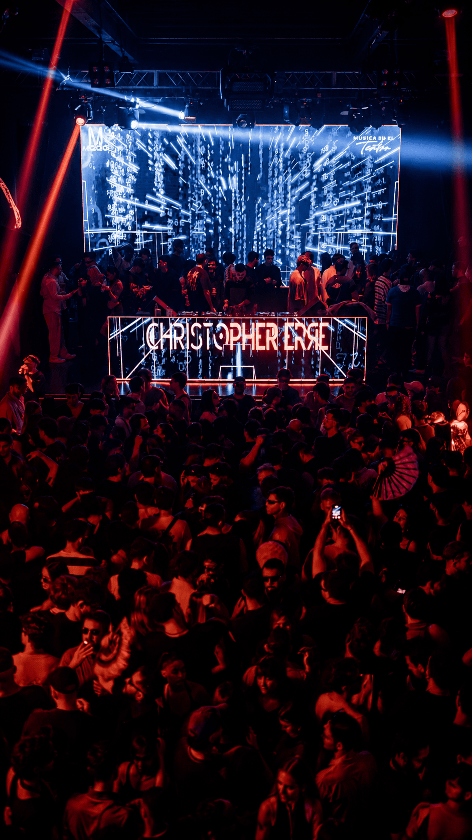 Audience view of Christopher Erre's illuminated booth and a crowded dance floor